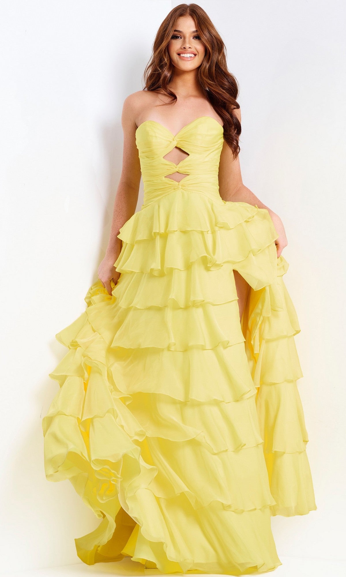 A woman smiles while holding out the skirt of the Jovani 47743 long yellow prom dress, featuring a strapless sweetheart neckline and ruffled A-line skirt.